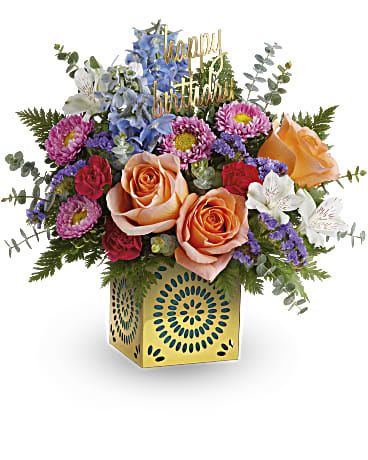 Colorful birthday flower arrangement with peach roses in a yellow cube vase and happy birthday pick
