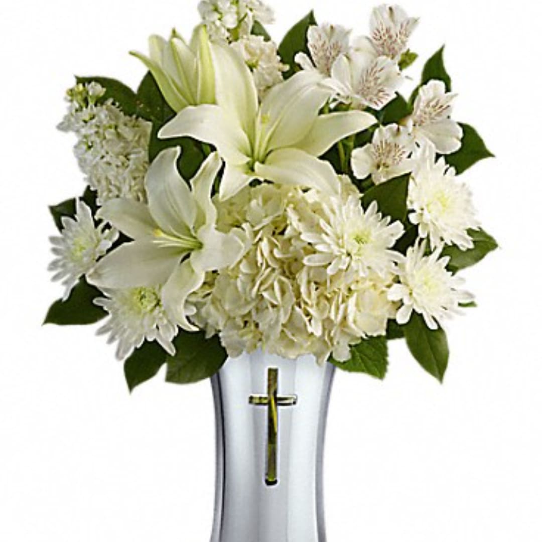 White lilies and daisies arranged in a silver vase with a cross
