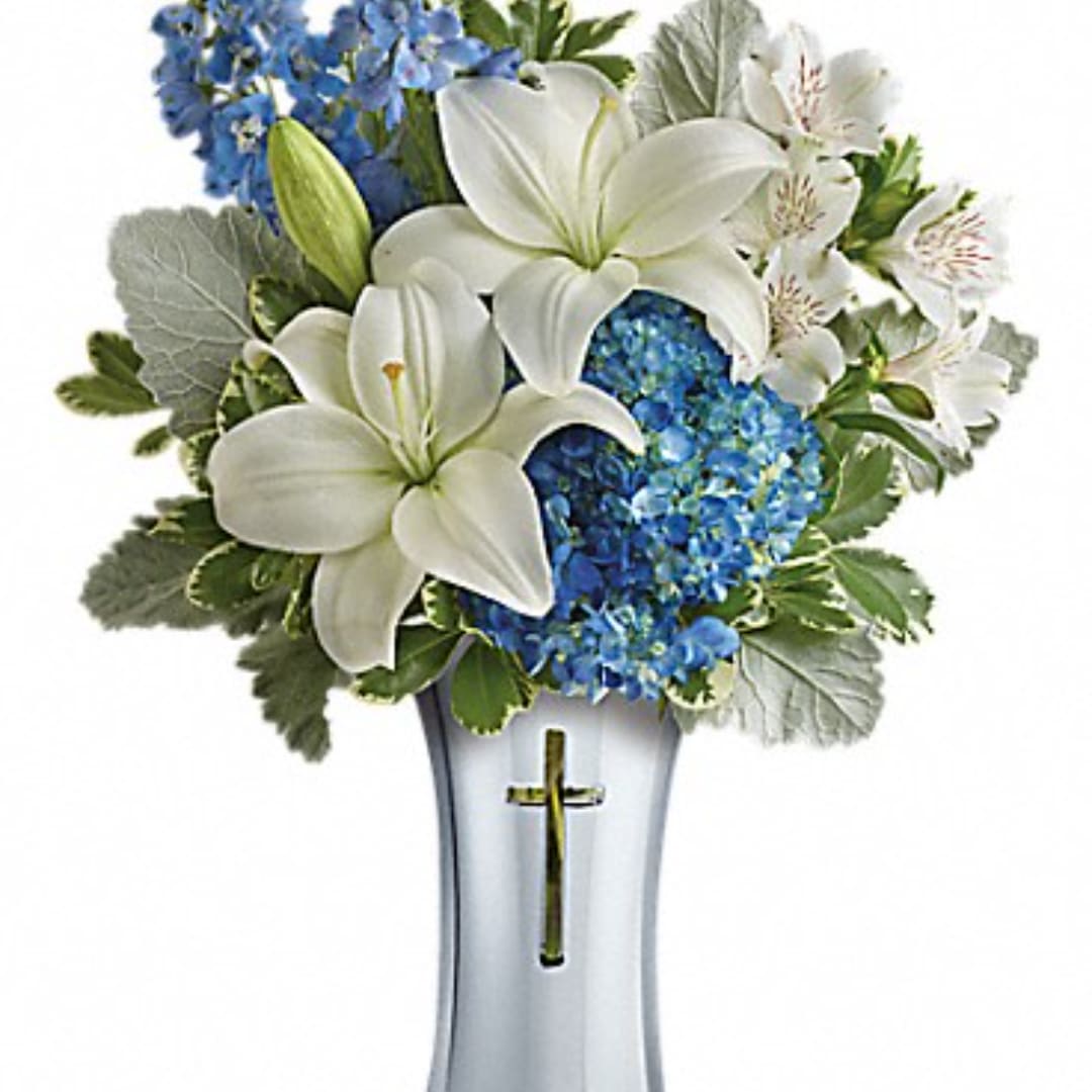 White lilies and blue hydrangeas in a silver vase with a cross