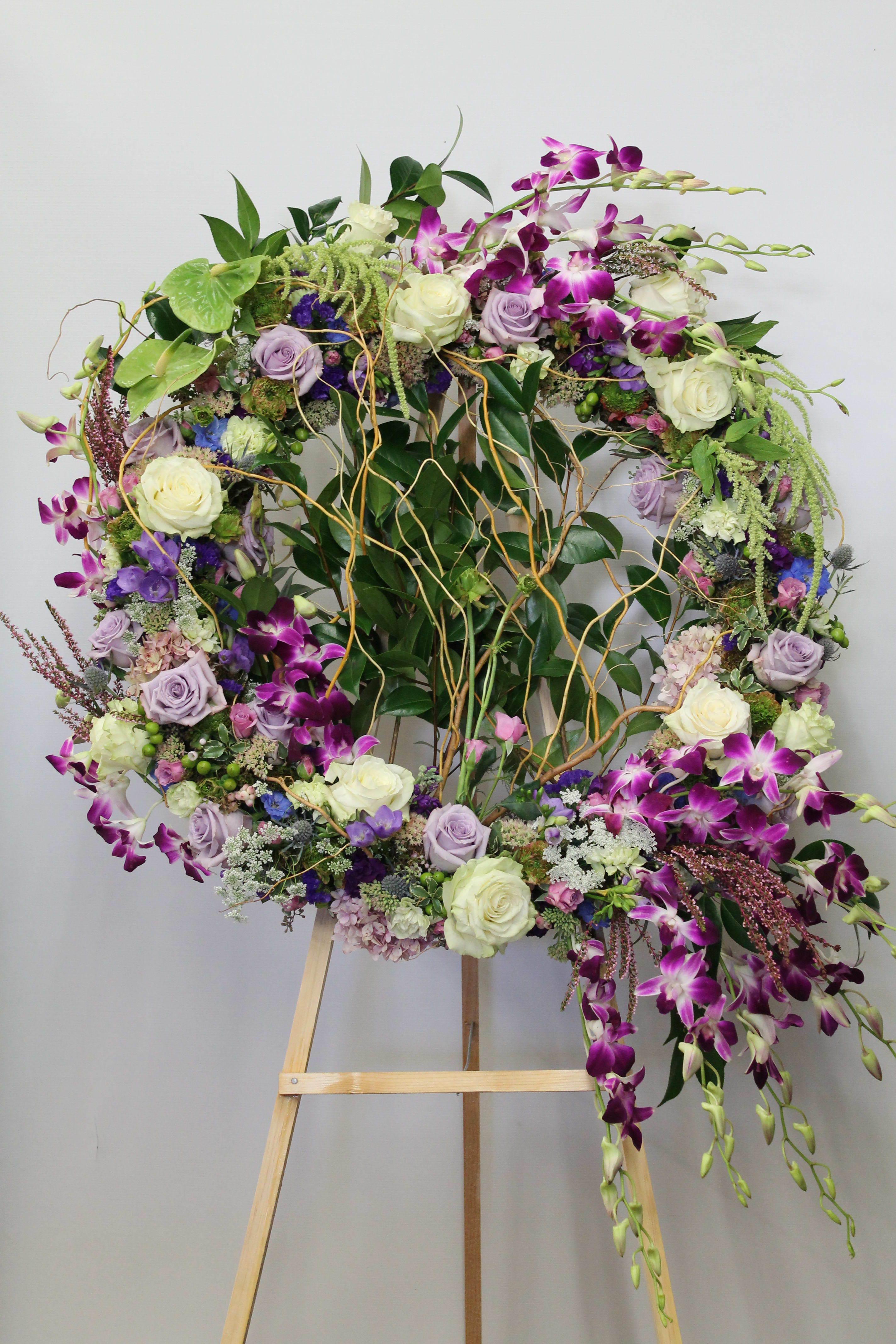 Large floral wreath on an easel with purple orchids and white roses