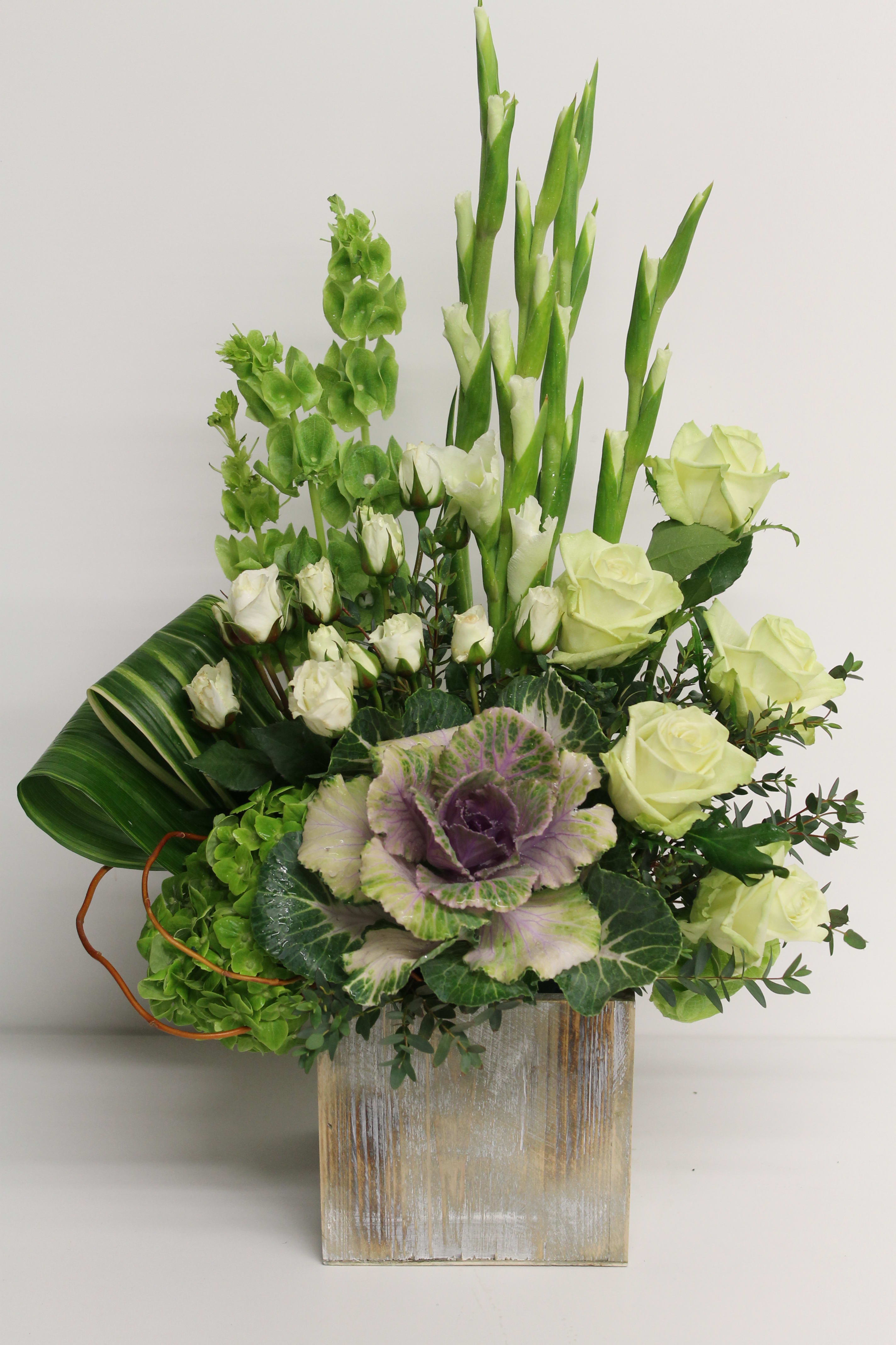 Green and white floral arrangement in a wooden box with roses and tall stems