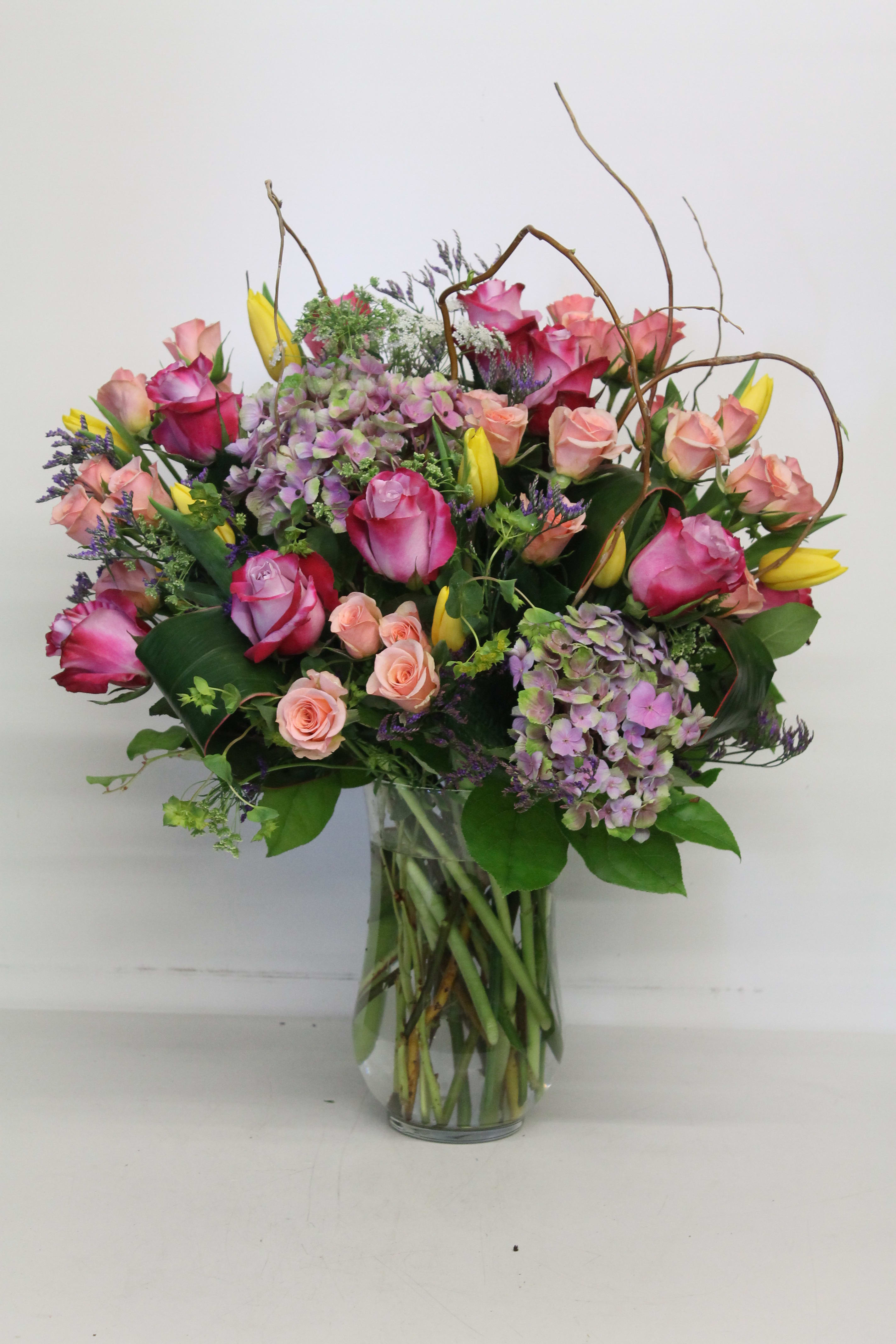 Mixed bouquet of pink roses, hydrangeas, and yellow tulips in a glass vase