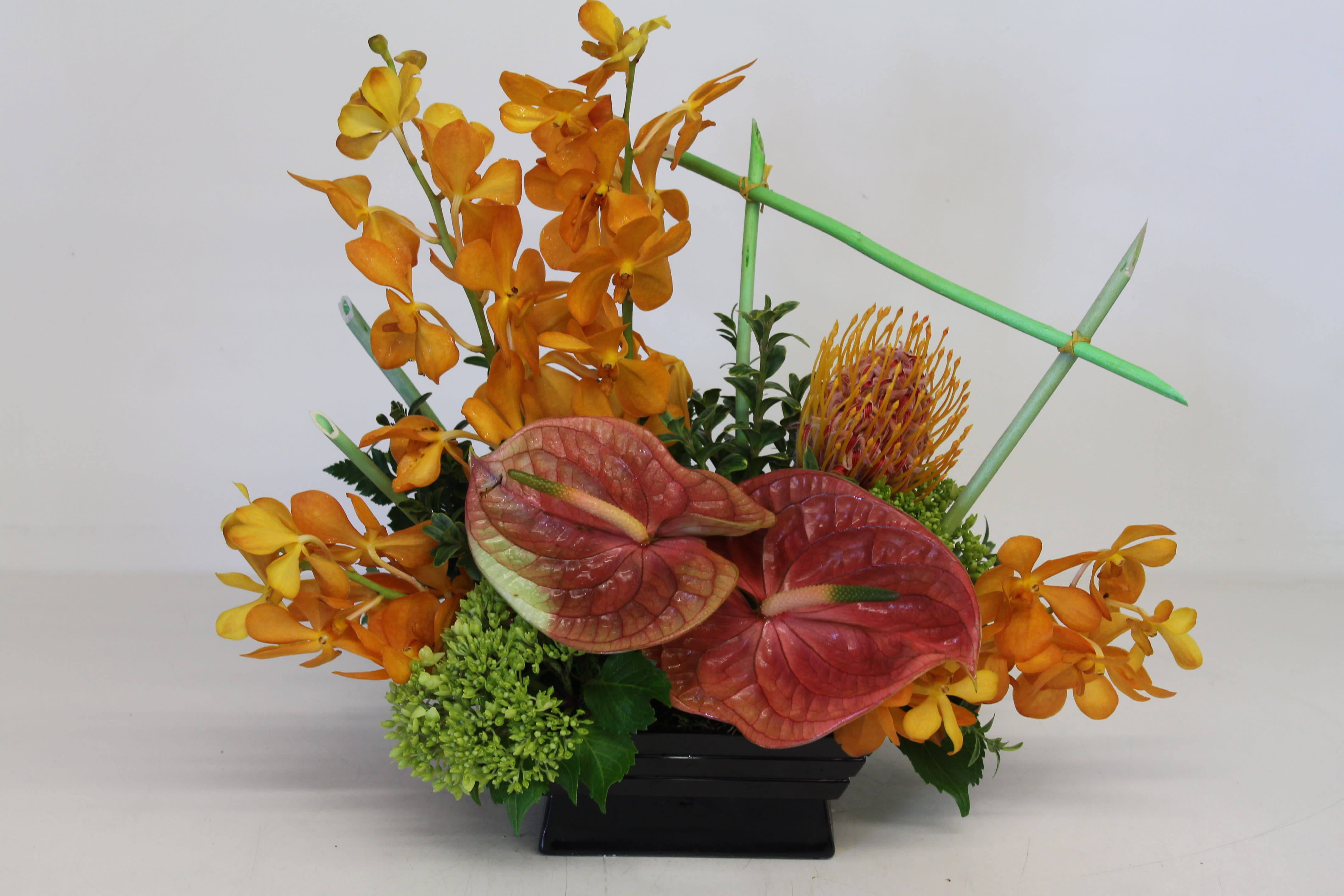 Orange orchid arrangement with red anthuriums in a black container