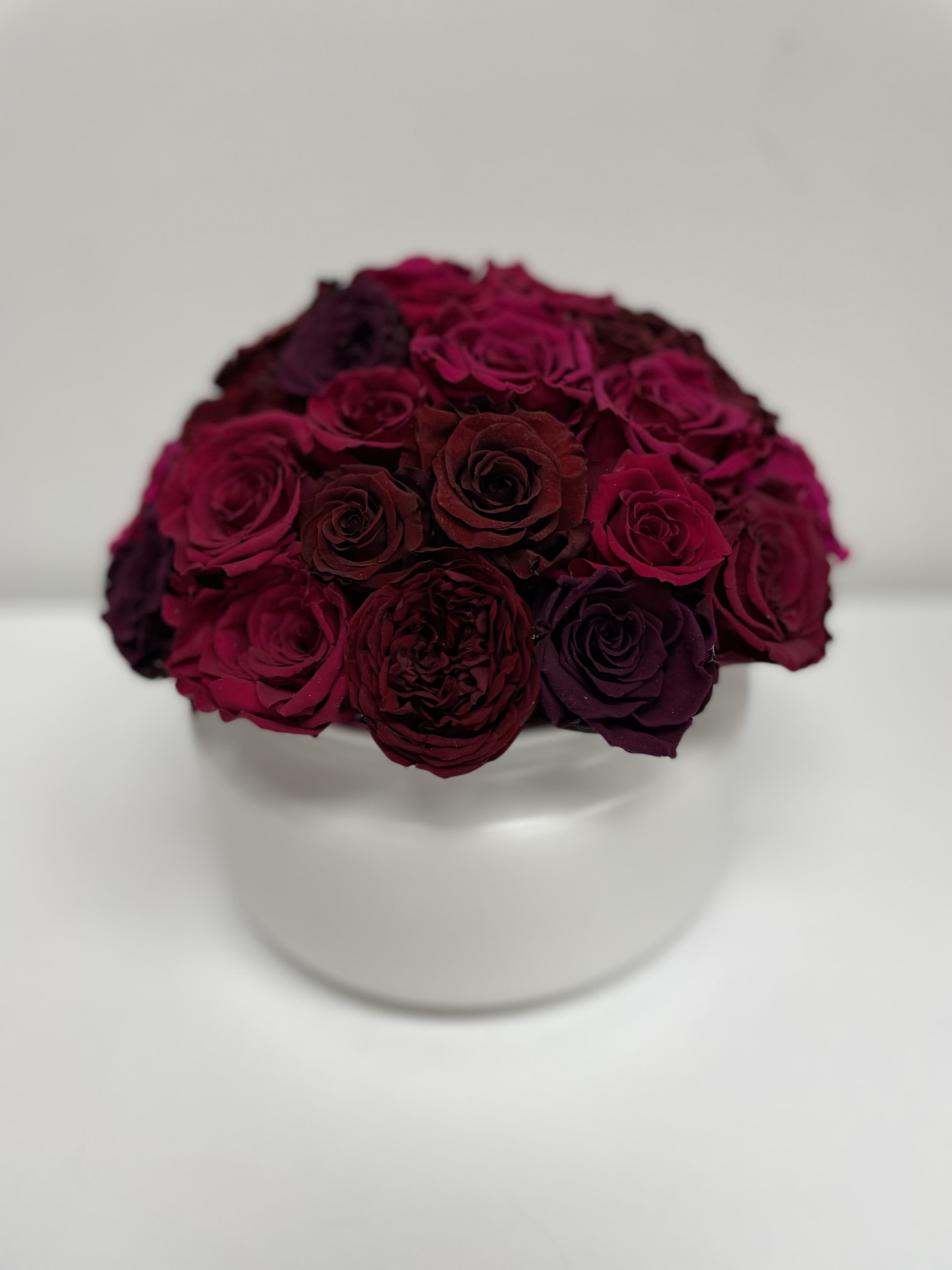 Compact bouquet of deep burgundy roses in a white vase