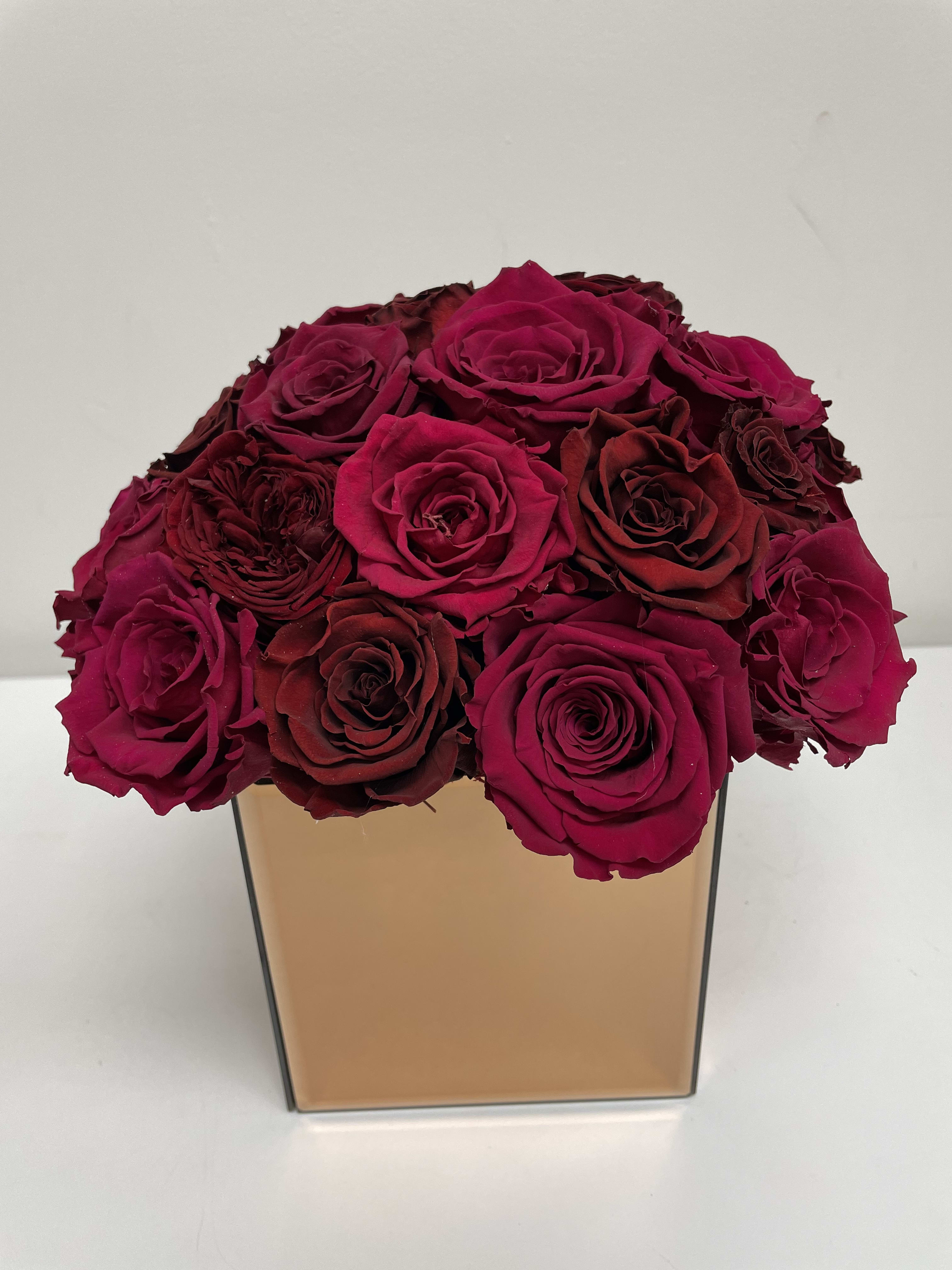 Bouquet of deep pink and burgundy roses in a square gold vase
