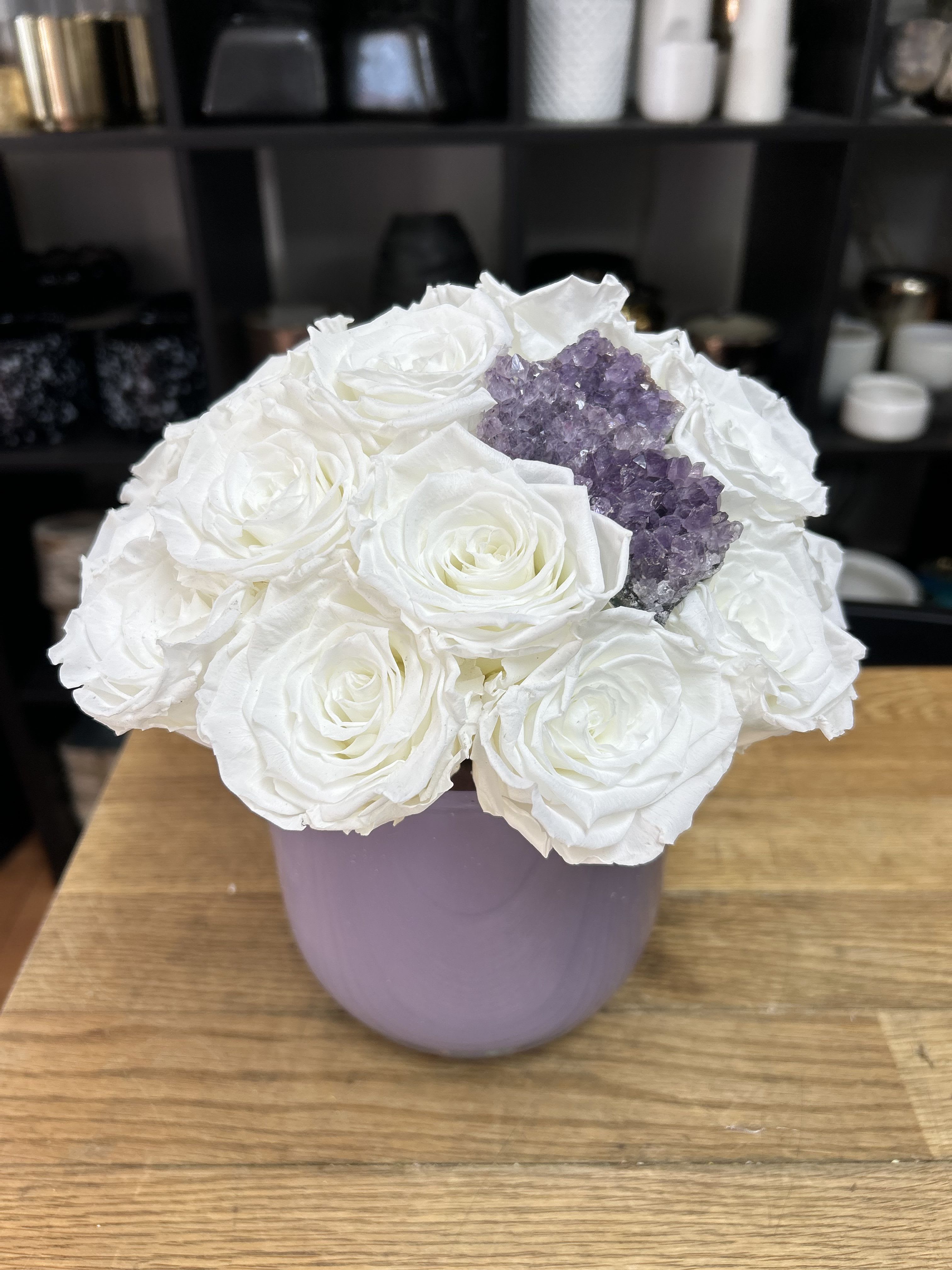 White roses arranged in a lavender vase with a purple crystal cluster