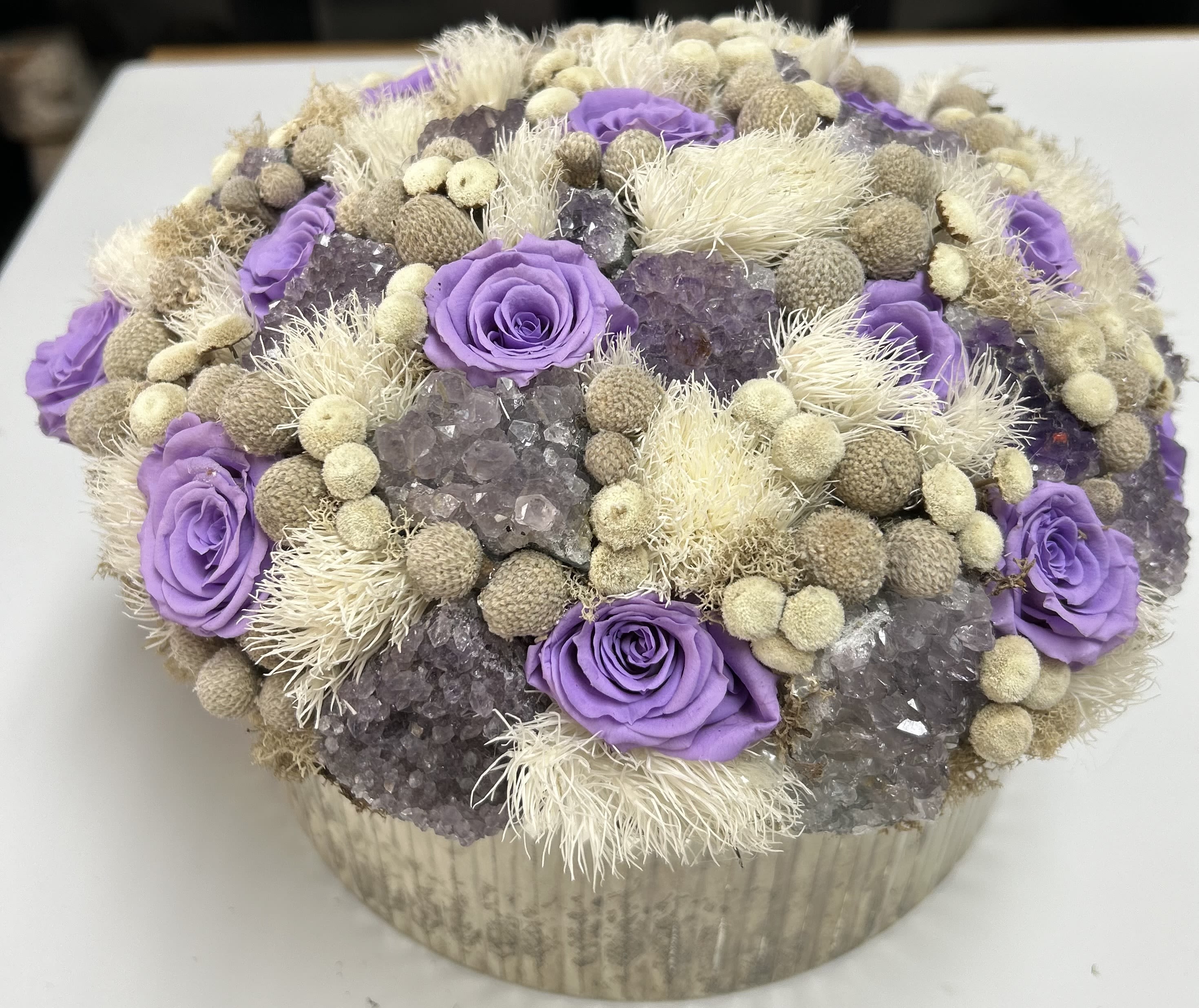 Purple roses arranged with dried beige accents in a round box