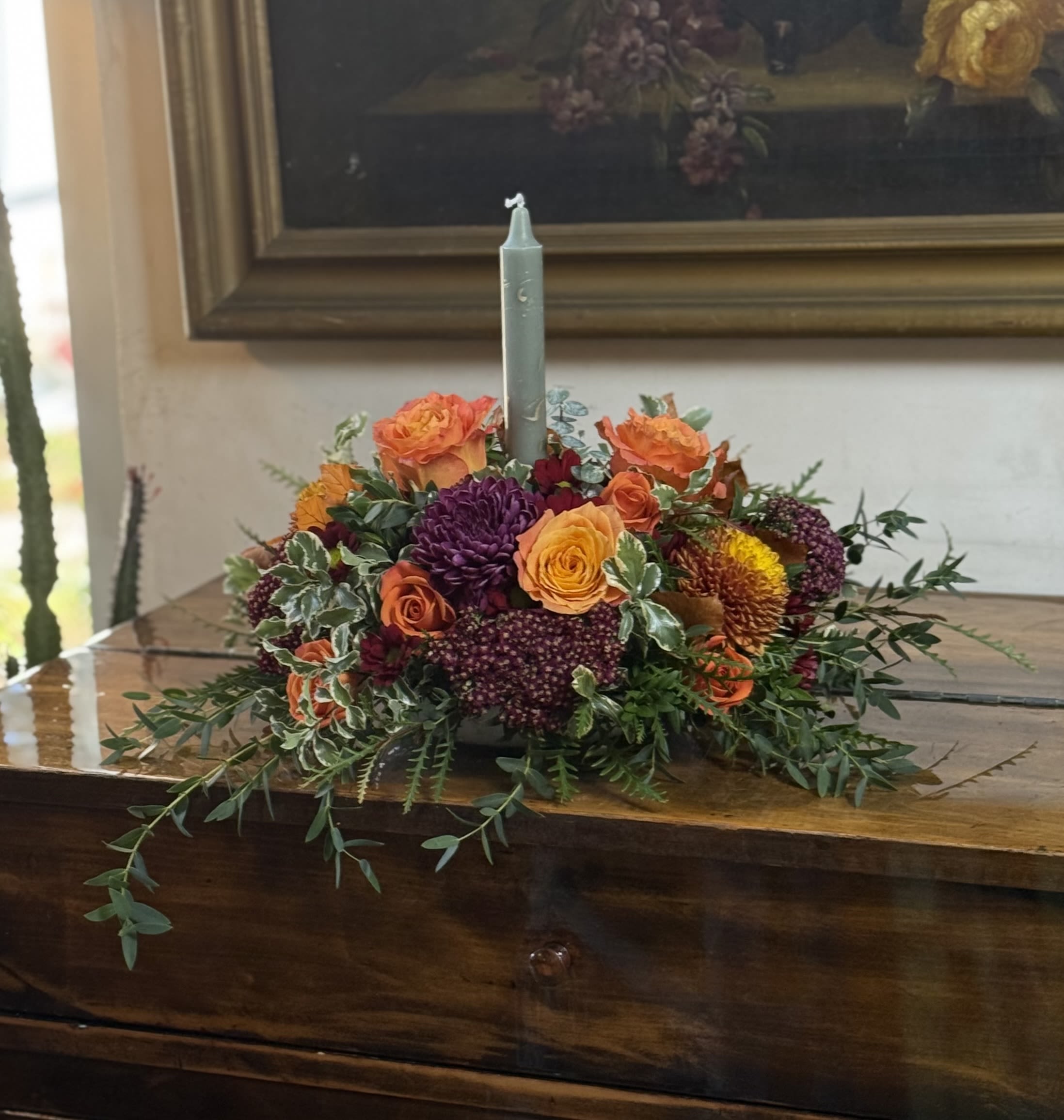 Low floral centerpiece with orange, yellow, and purple blooms around a candle