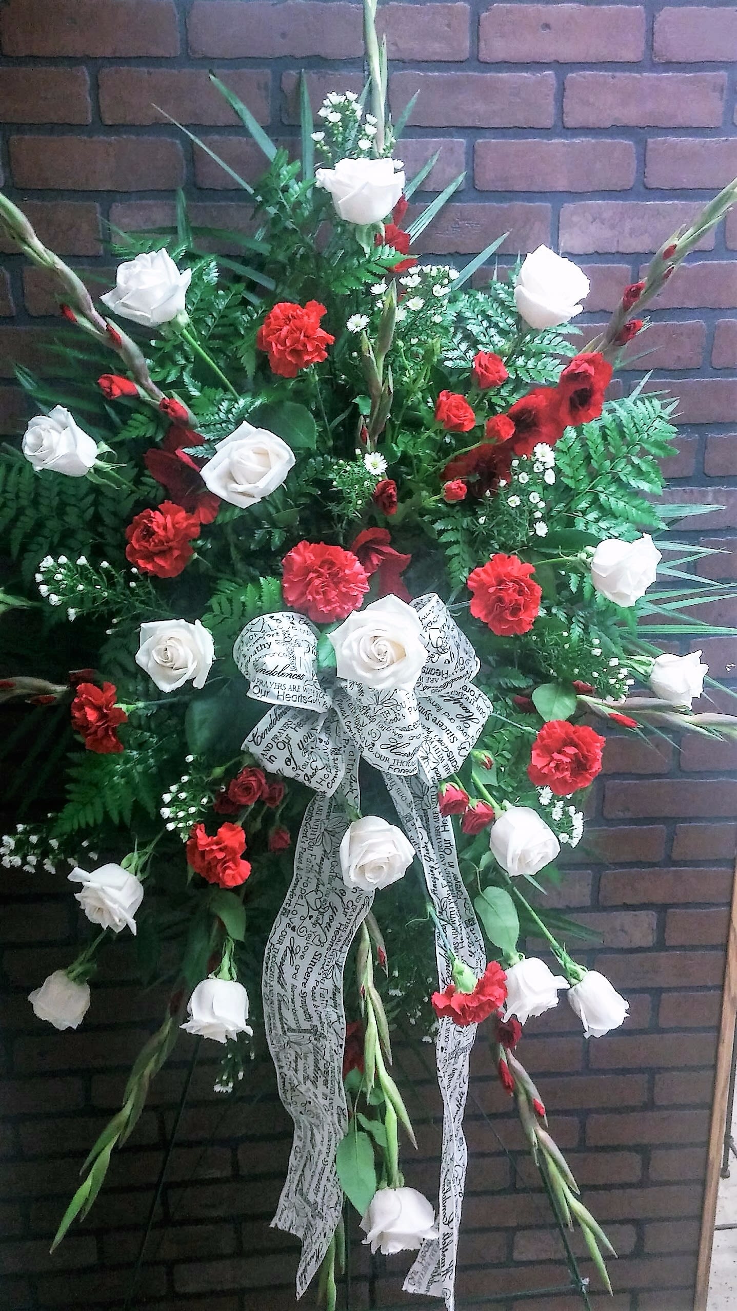 Standing floral spray with red and white roses and carnations, accented by a printed ribbon bow