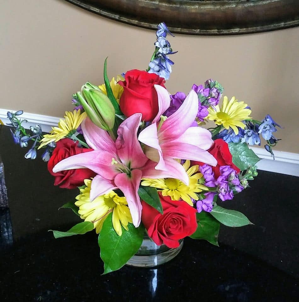 Just Happy - A round cylinder vase filled with lilies, roses, stock and other beautiful blooms