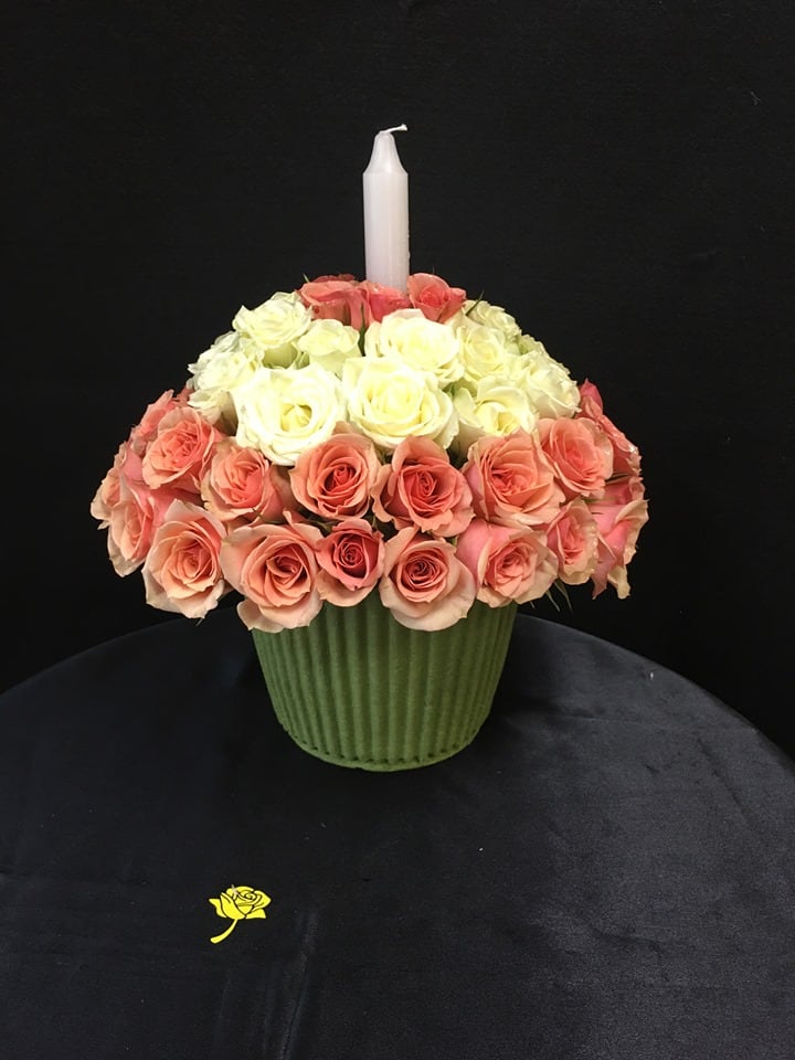 Pink and white rose arrangement in a green vase with a white candle
