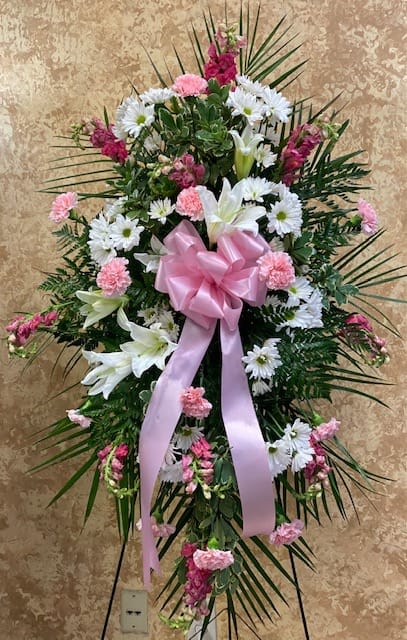 Standing floral spray with white lilies, daisies, and pink carnations, tied with a pink bow