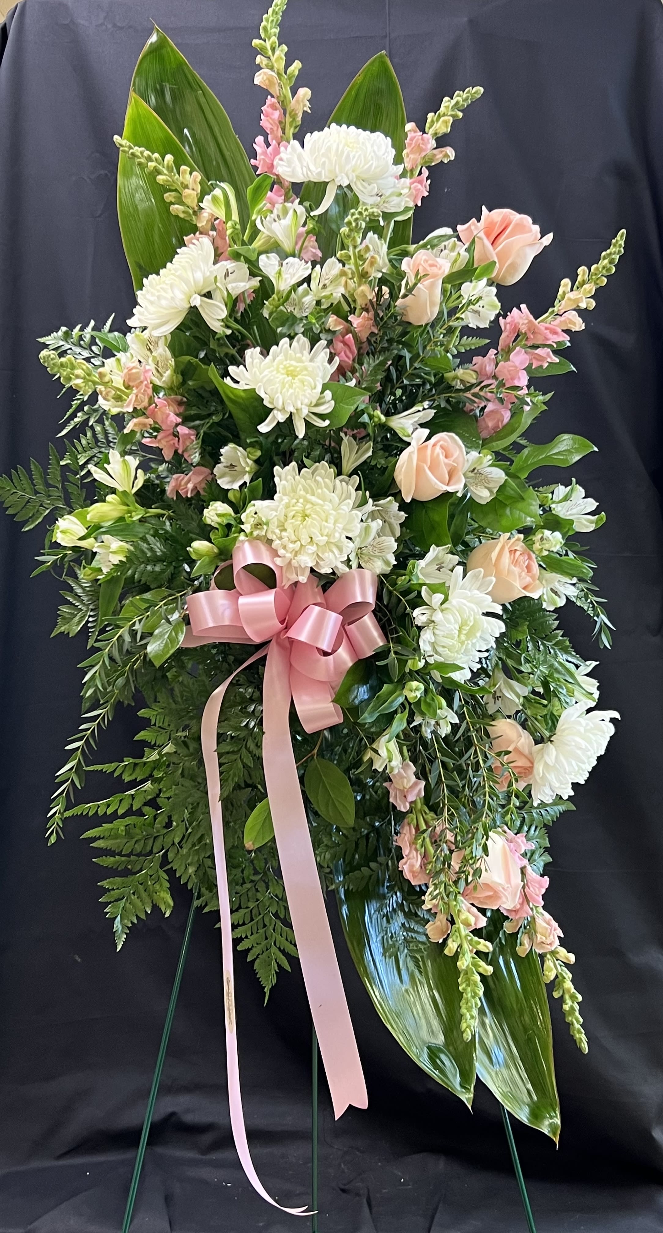 Standing floral spray with white and peach flowers and a pink ribbon