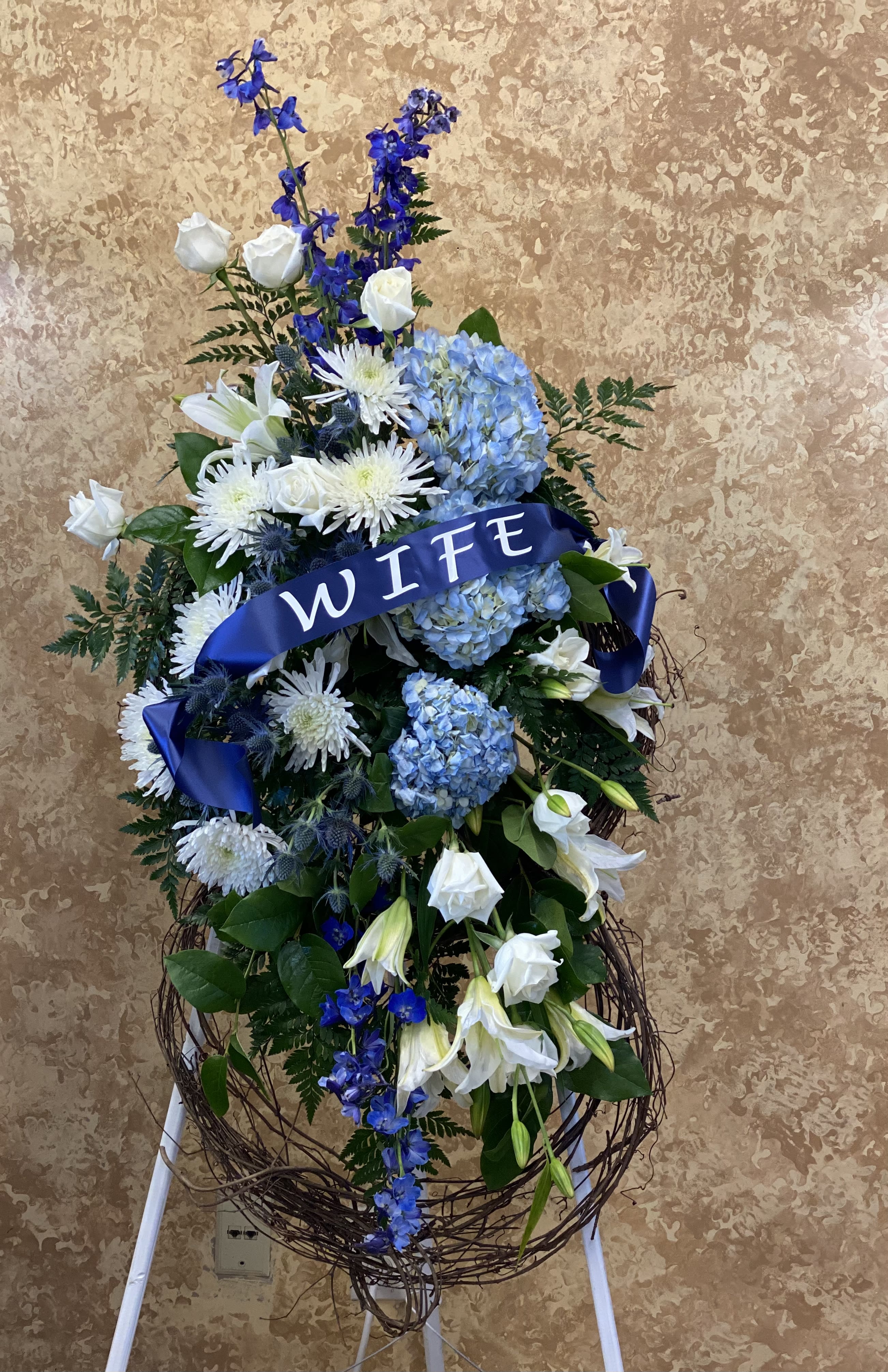 Large blue and white floral standing spray with a ribbon reading WIFE