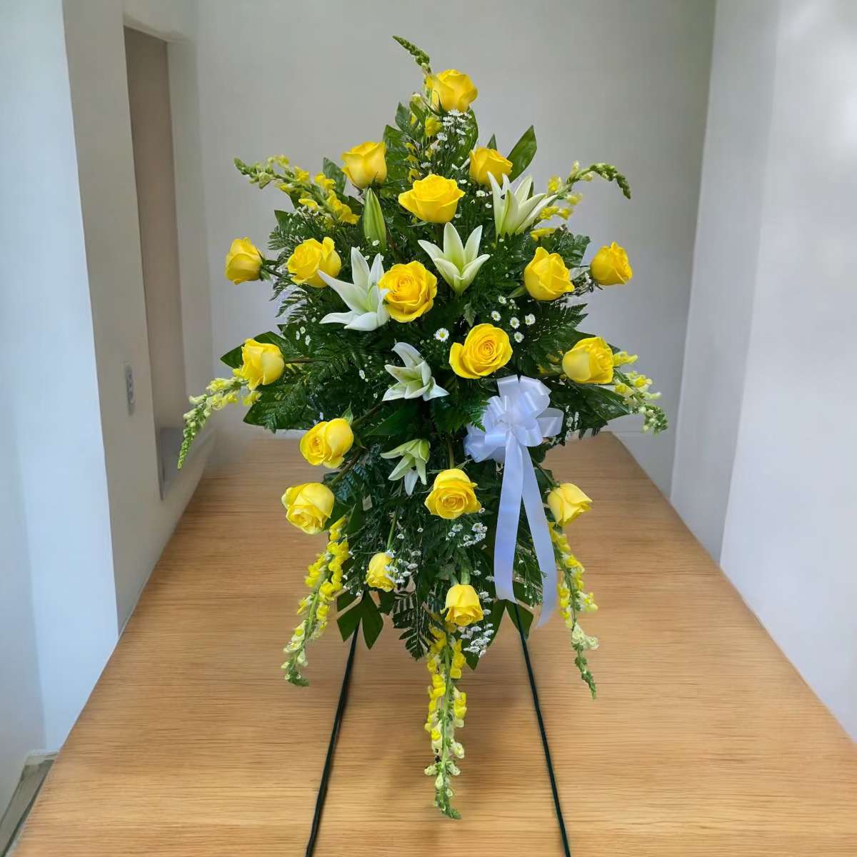 Strong Ties Friendship Spray - What a wonderful way to express your love and the string ties you had with your friend or loved one.  This spray is designed with Yellow Roses, snapdragons, and white lilies. Displayed on a easel.