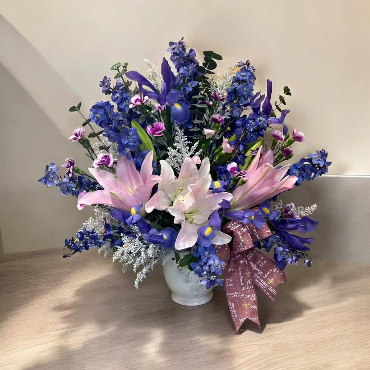 Tender Thoughts - In times of sorrow for the loss of a loved one send Tender Thoughts to the family. Makes a wonderful gift for the service or home. Designed in our ceramic container with lilies, blue delphinium, irises and other blooms.