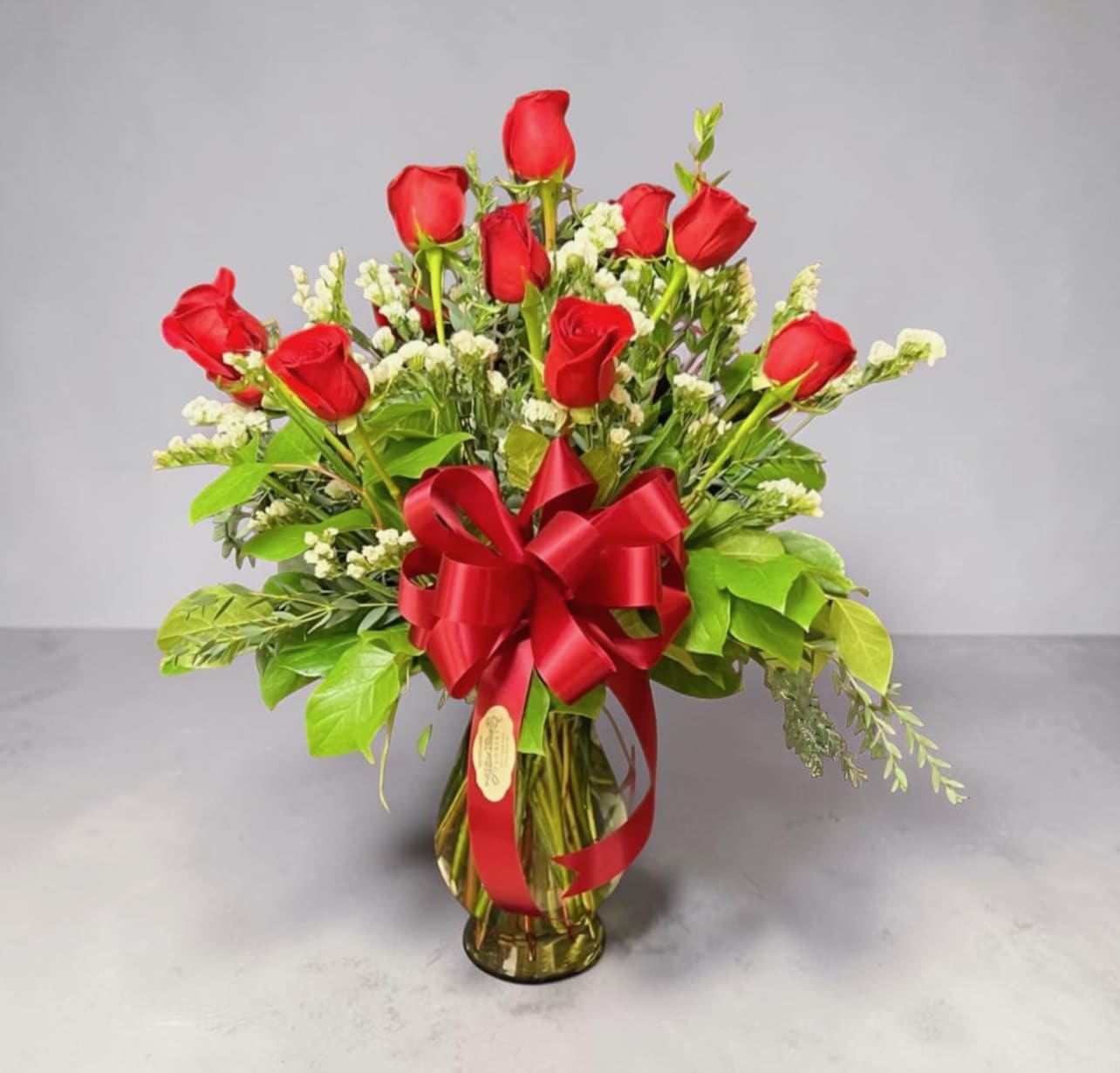 Dozen of Love - Share the love 12 times over with our beautiful red roses.  Standard shown, Designed in a clear glass vase with three different types of greenery and filler.