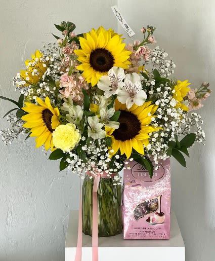 Bouquet of sunflowers and white flowers in a glass vase with a pink gift box
