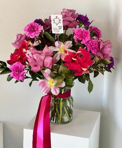 Pink and red mixed flower bouquet in a glass vase with a ribbon