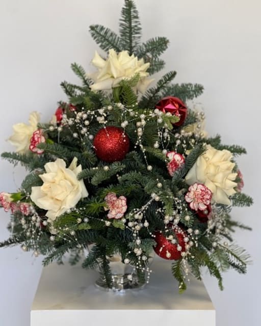 Christmas arrangement with white flowers, red ornaments, and evergreen branches in a glass vase