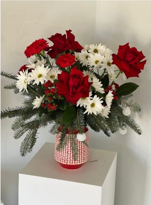 Red roses and white daisies in a red-and-white vase with evergreen branches