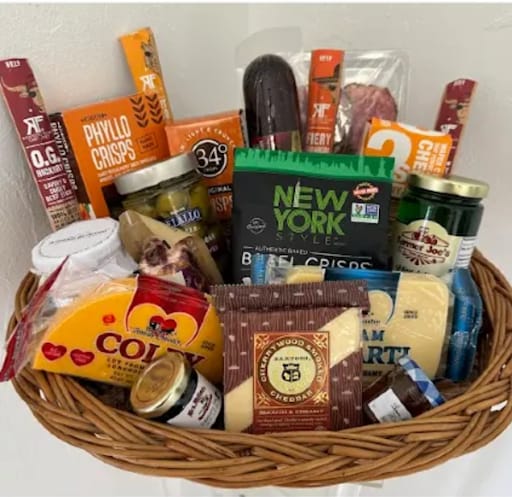 Gift basket filled with assorted snacks, cheeses, and jars in a wicker basket