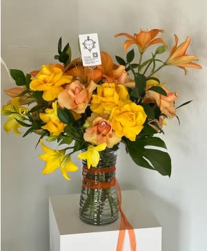 Orange and yellow lilies arranged in a glass vase with ribbon