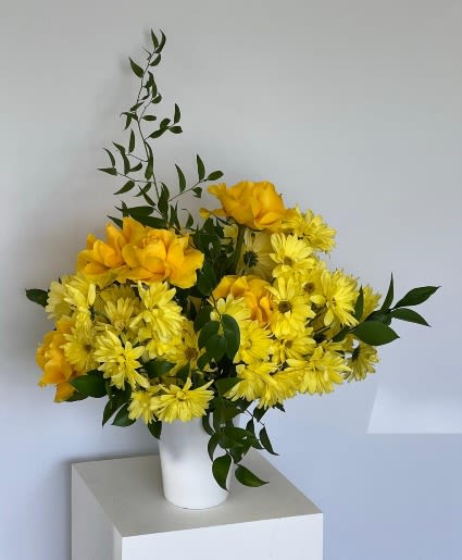 Yellow flowers arranged in a white vase with dark green foliage