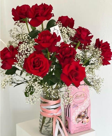 Bouquet of red roses with baby's breath in a glass vase beside a pink candy box