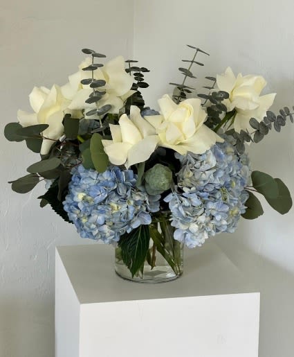 Blue hydrangeas and white flowers in a clear glass vase