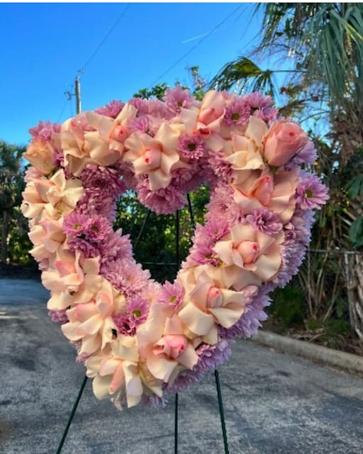 Heart-shaped floral wreath with pink and peach blooms on a stand