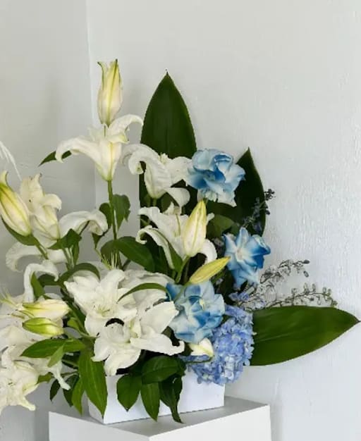 White lilies and blue hydrangeas arranged in a white box