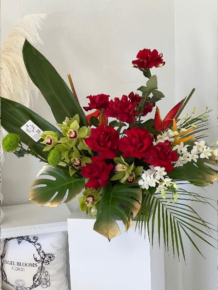 Red roses and green orchids arranged with tropical leaves in a white vase.