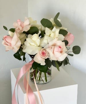Bouquet of pale pink and white roses in a glass vase with a pink ribbon