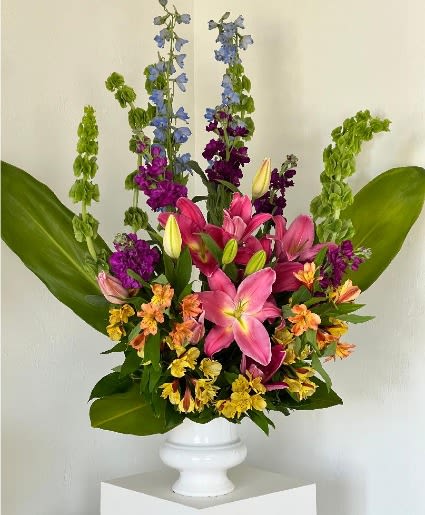 Tall mixed bouquet of lilies and purple flowers in a white pedestal vase