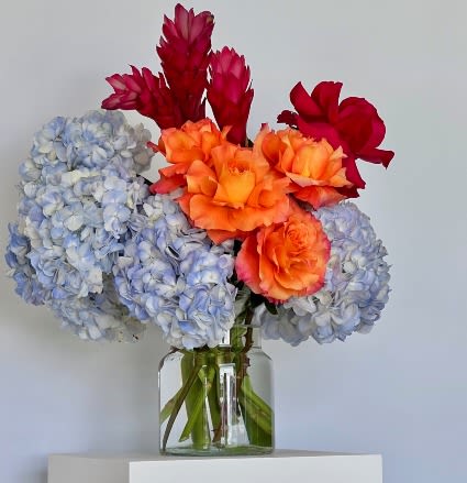 Bouquet of blue hydrangeas and orange-red flowers in a glass vase