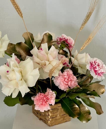 Pink and white floral arrangement in a woven basket with wheat stems