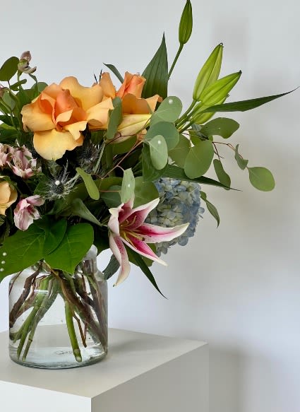 Bouquet of peach roses, lilies, and blue hydrangea in a glass vase