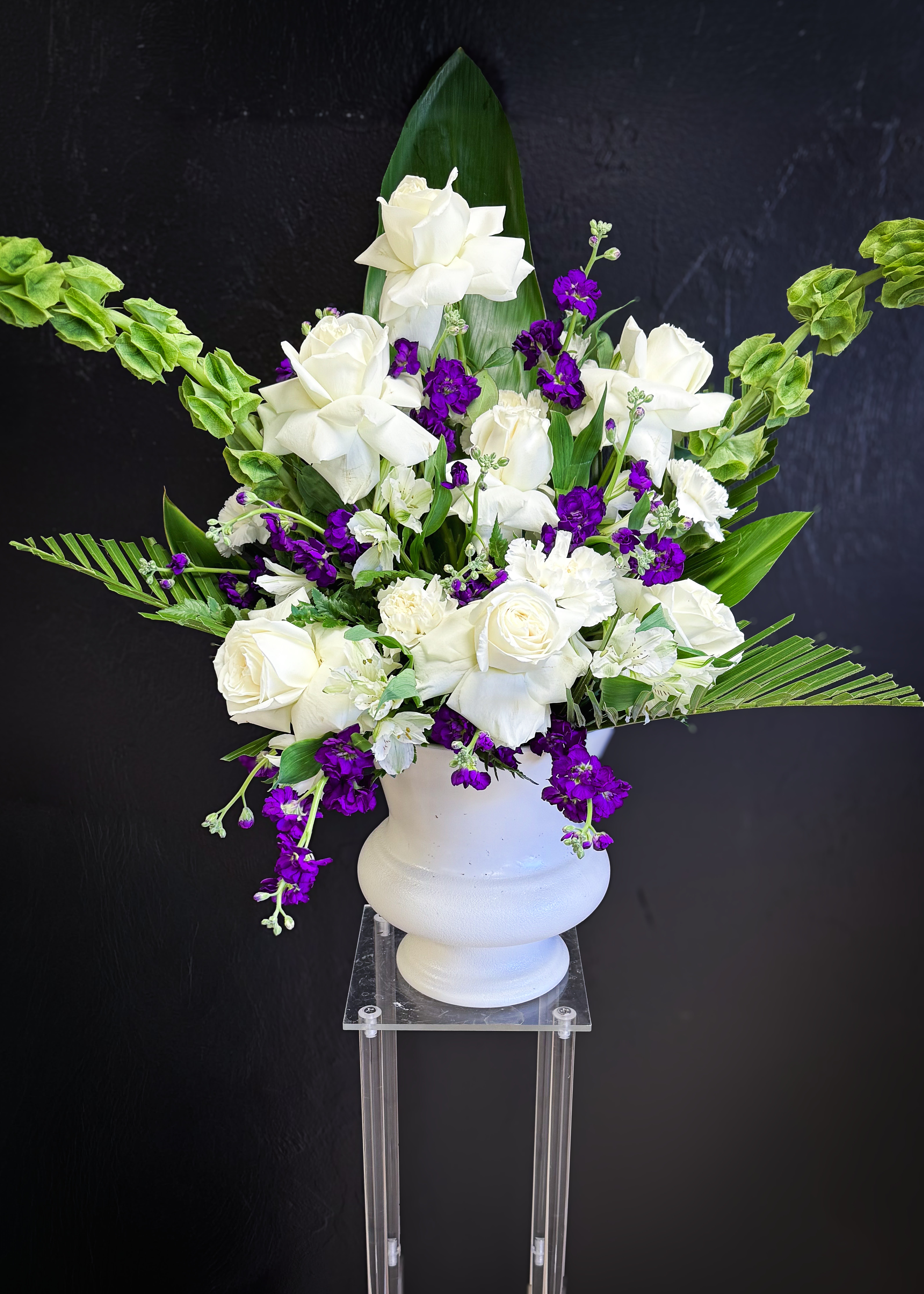 White roses and purple flowers arranged in a white urn vase