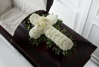White floral cross arrangement on a dark casket