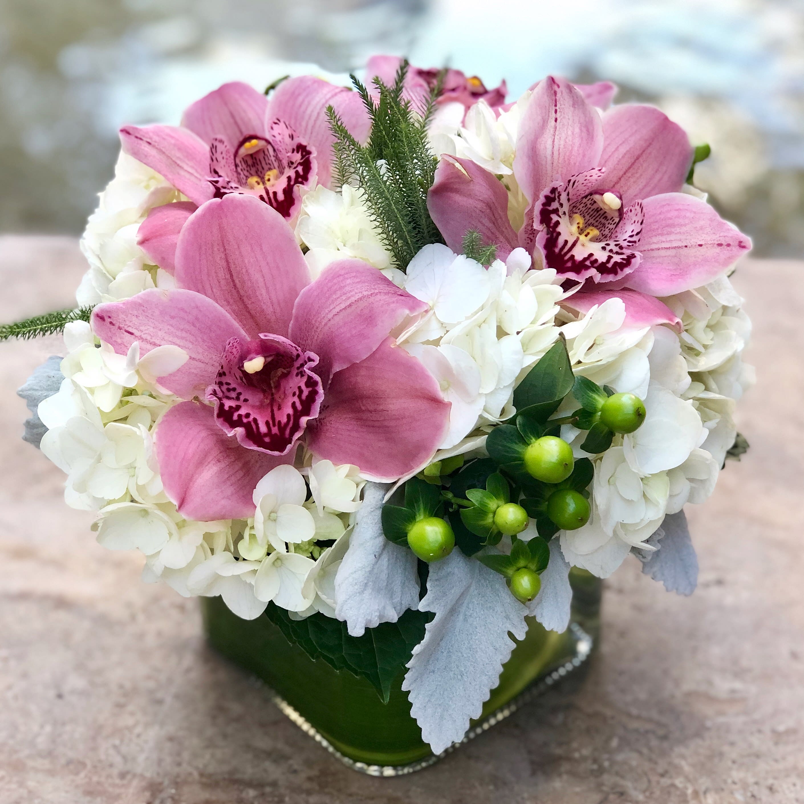 Pink orchids and white hydrangeas in a green glass vase