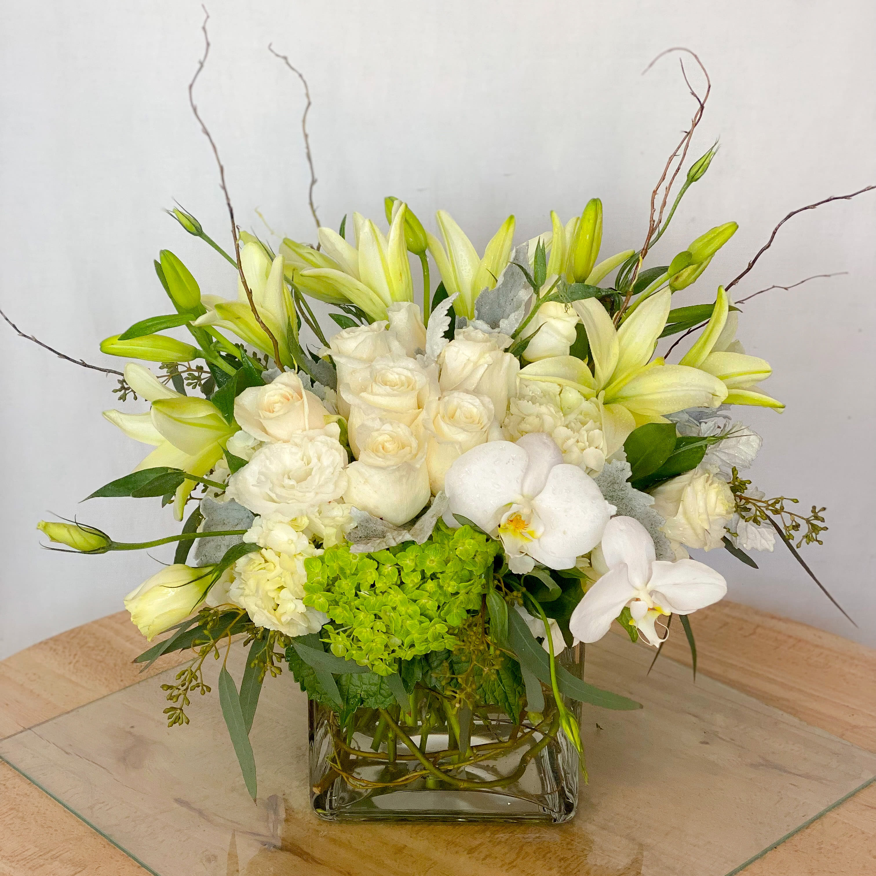 White and pale yellow floral arrangement in a square glass vase