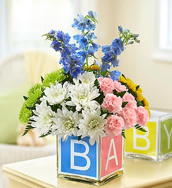 Baby Block Cube - Product ID: 95208  EXCLUSIVE Spell out your best wishes on the birth of their new baby with this truly original, totally adorable arrangement. Inside a stylish cube vase, our florists gather frilly carnations, assorted playful poms and striking delphinium. The vase is lined with a foam insert that spells out BABY to help you congratulate the new parents perfectly. Abundant, brightly colorful gathering of carnations, poms and delphinium, accented with fresh leather leaf Designed by our florists in a clear glass cube vase wrapped with a colorful ribbon with the letters B-A-B-Y; vase measures 5"H x 5"D Large arrangement measures approximately 19"H x 12"L Medium arrangement measures approximately 17"H x 11"L Small arrangement measures approximately 15"H x 10"L Our florists select the freshest flowers available so colors and varieties may vary