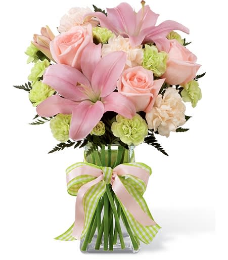 Pink lilies and roses in a glass vase with a striped ribbon