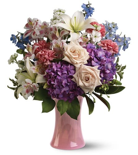 Mixed bouquet of roses, lilies, hydrangeas, and carnations in a pink vase