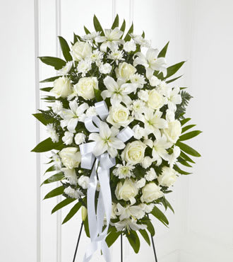White floral standing spray with roses and lilies on a white ribboned easel
