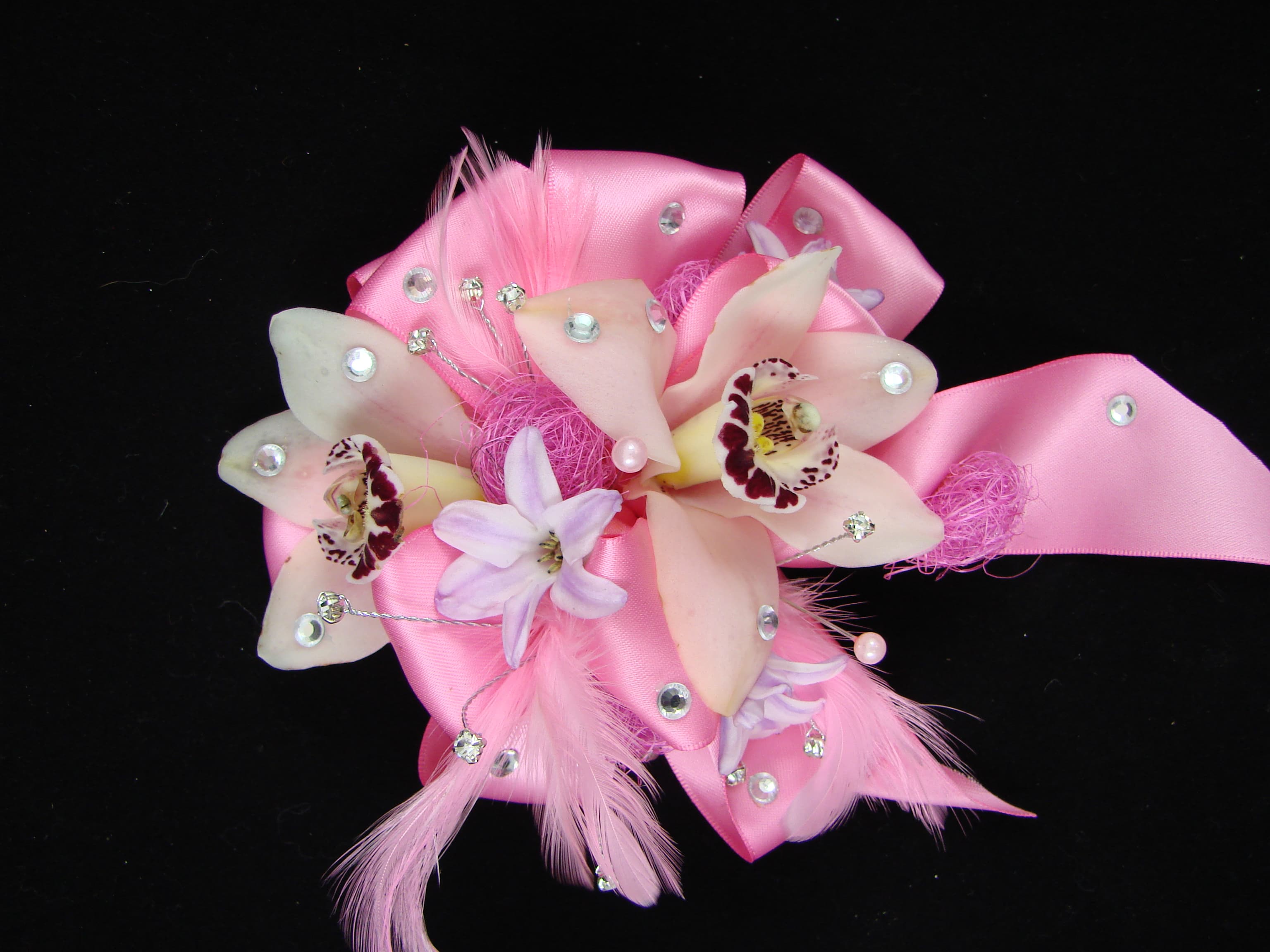 Pink ribbon corsage with pale orchid blooms and decorative feathers