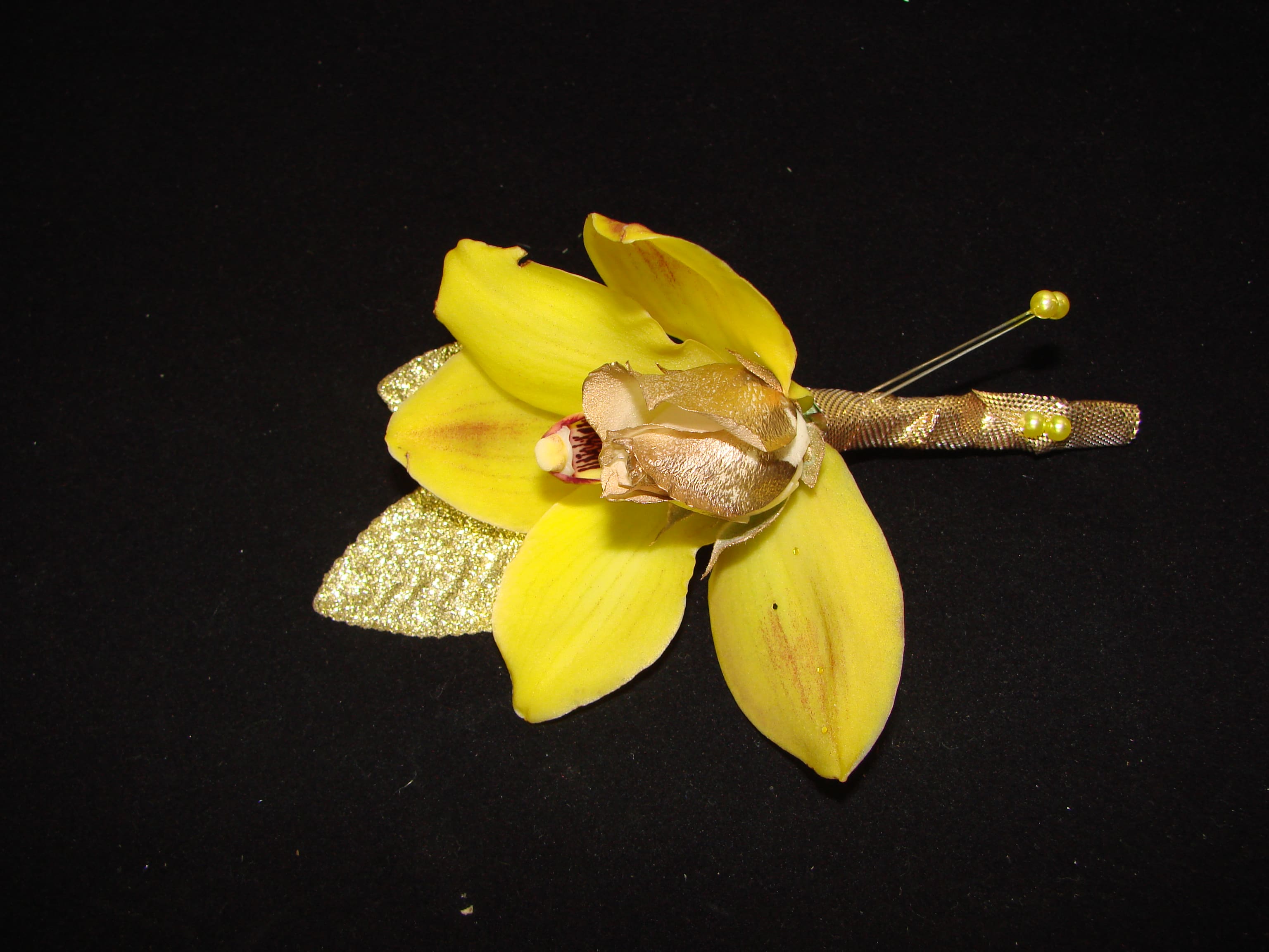Yellow orchid boutonniere with gold ribbon on a black background