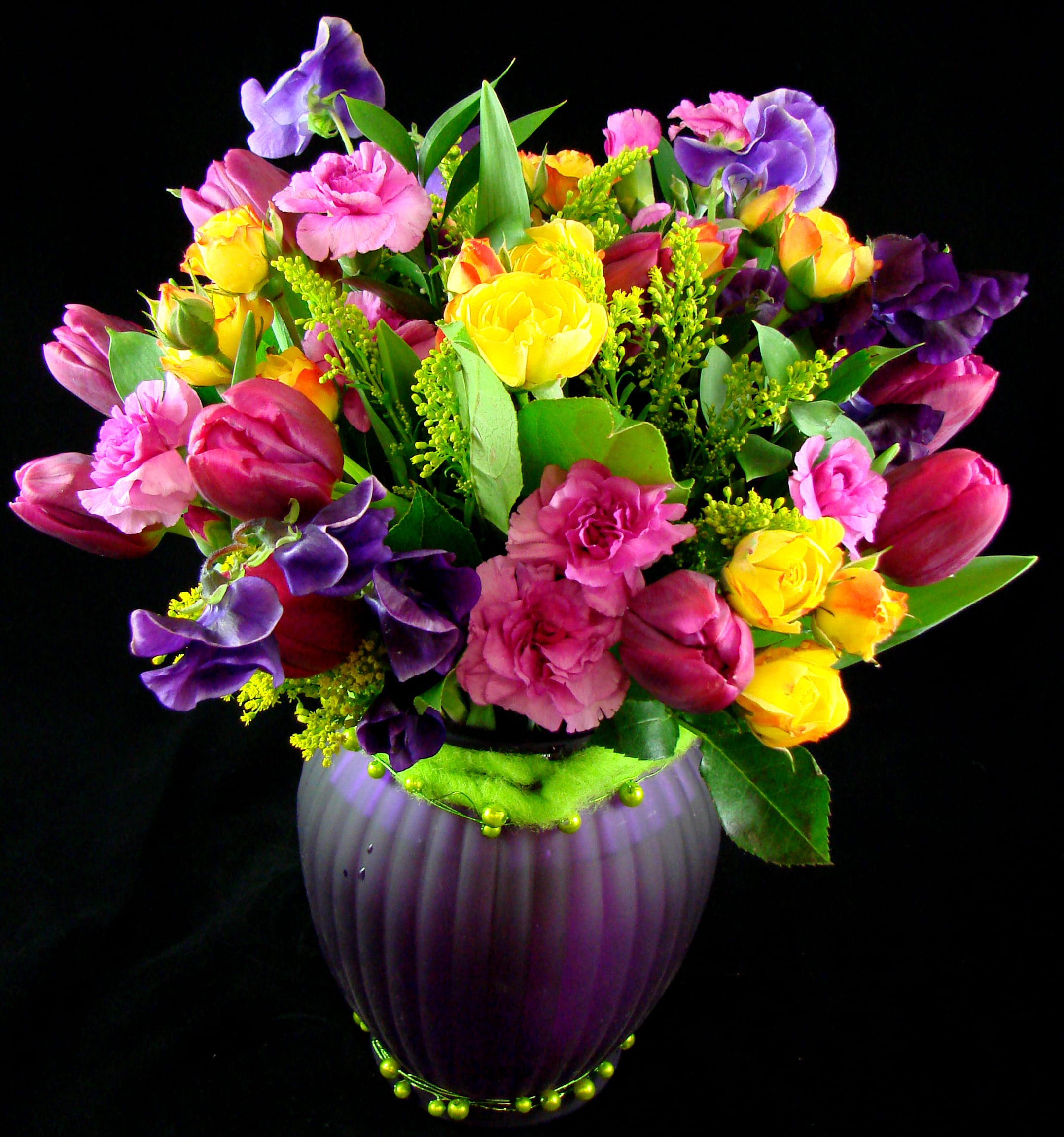 Colorful bouquet of tulips, roses, and carnations in a purple vase