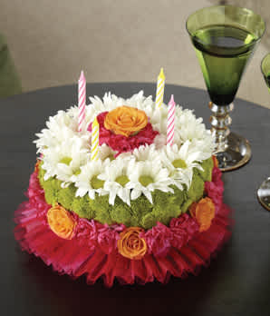 Round floral cake with candles and white daisies on a table